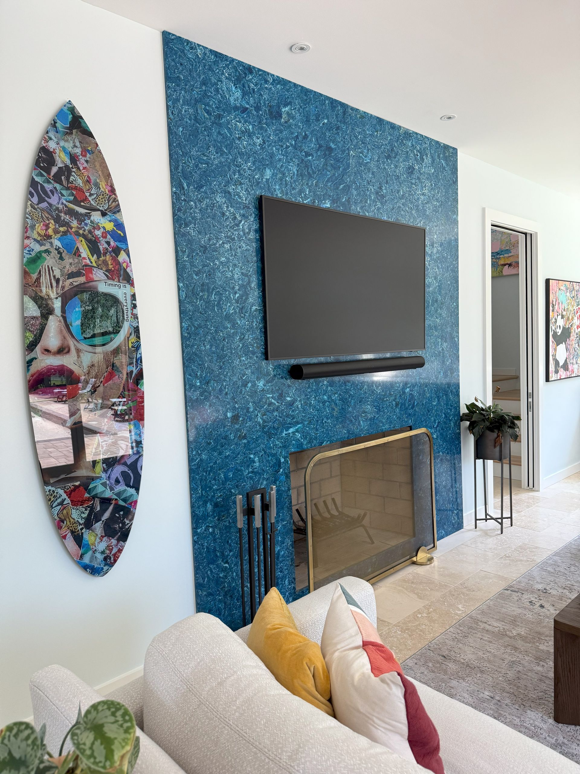 Living room with blue mosaic fireplace, TV, surfboard art, and white sofa.