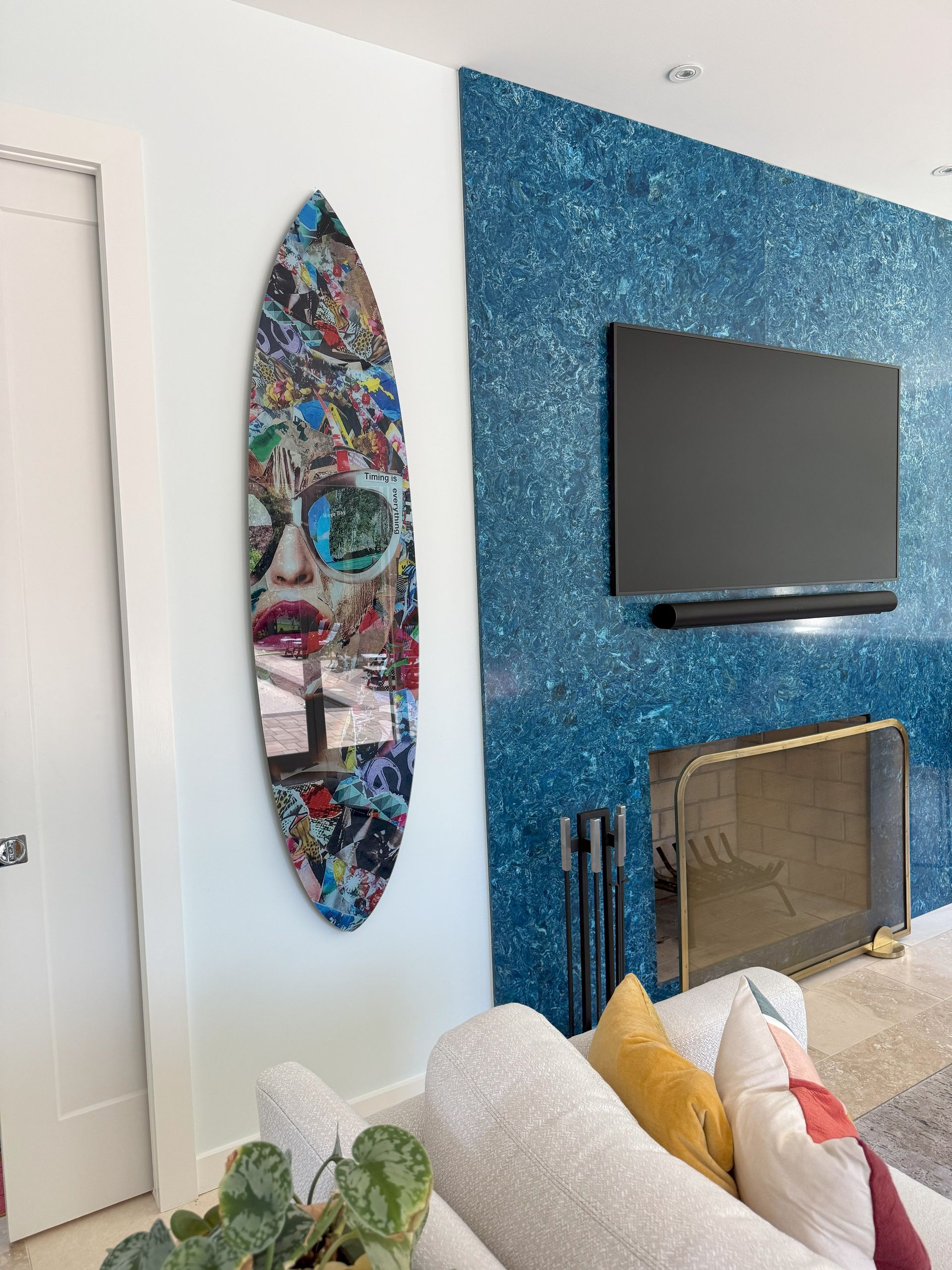 Surfboard art, face design, mounted on white wall. Blue textured wall with TV, fireplace in room.