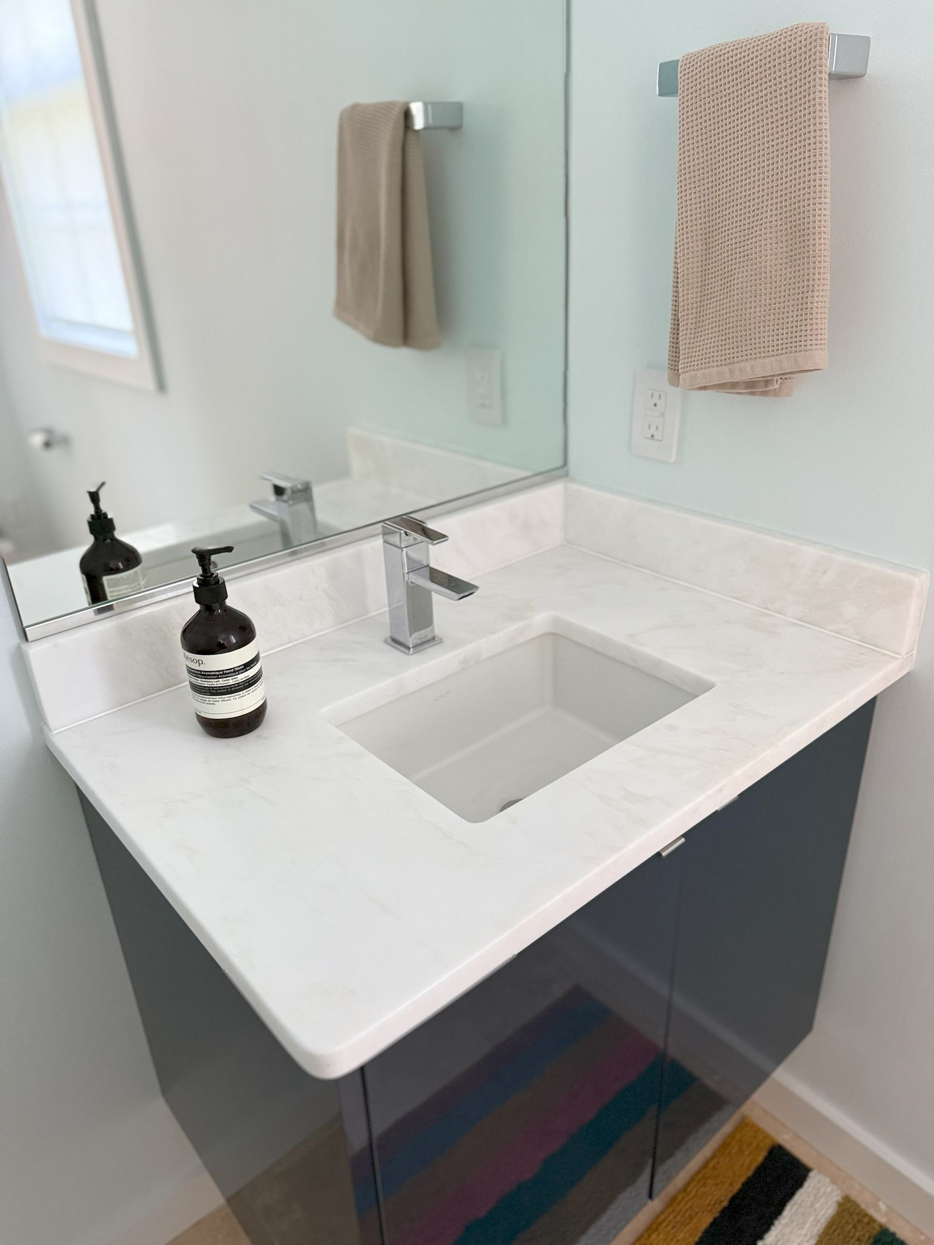 Modern bathroom vanity with white countertop, rectangular sink, and mirror; towel bar with tan towel.