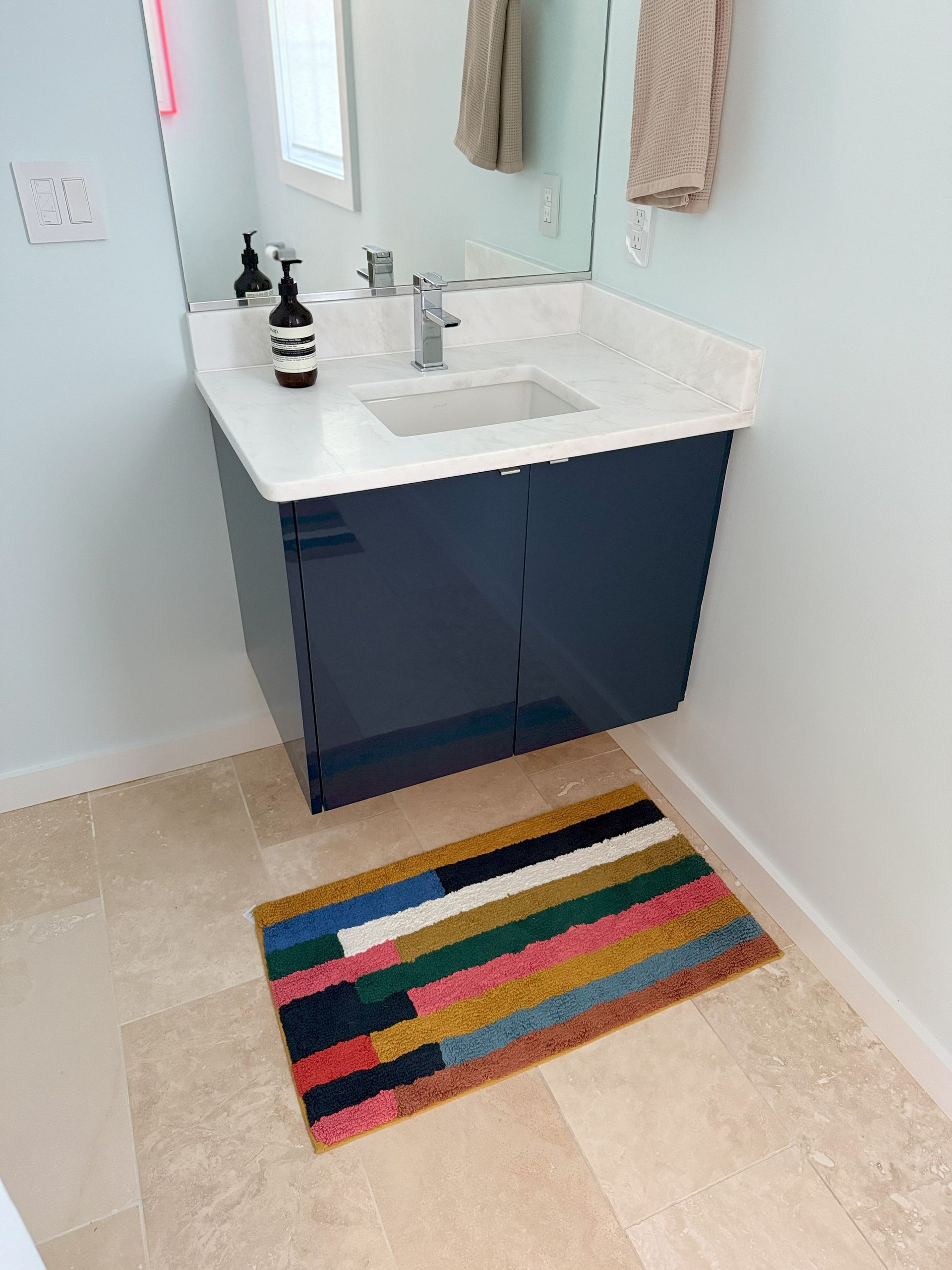 A blue floating bathroom vanity with a colorful rug, a sink, and mirror.