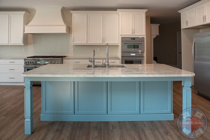 A kitchen with white cabinets and a blue island in the middle.