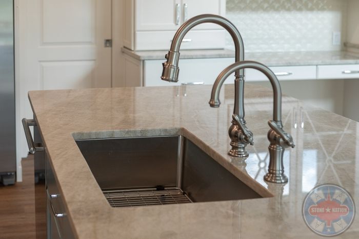 A kitchen sink with two faucets on a granite counter top.