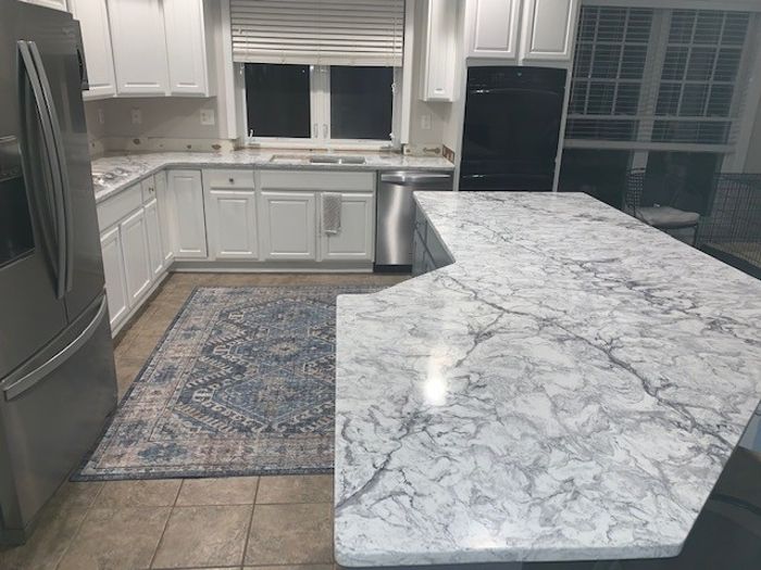 A kitchen with white cabinets , marble counter tops , stainless steel appliances and a rug.
