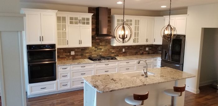 A kitchen with white cabinets , granite counter tops , stainless steel appliances and a large island.