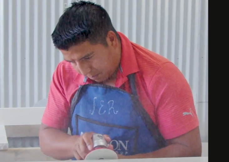 A man in a red shirt and blue apron is reading a book.