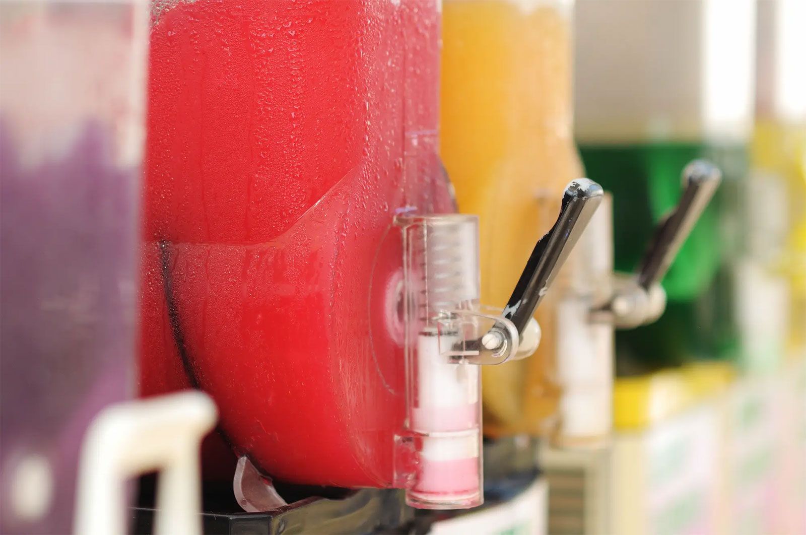 Row of colorful frozen drink dispensers with metal levers in a shop