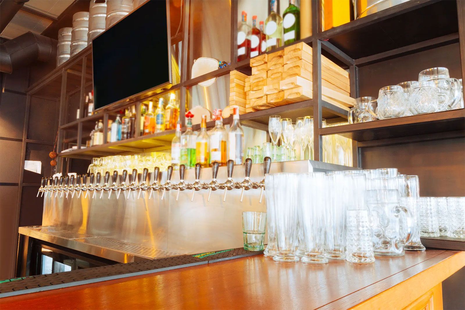 Empty bar counter with rows of hanging wine glasses and stacked glassware under warm lighting