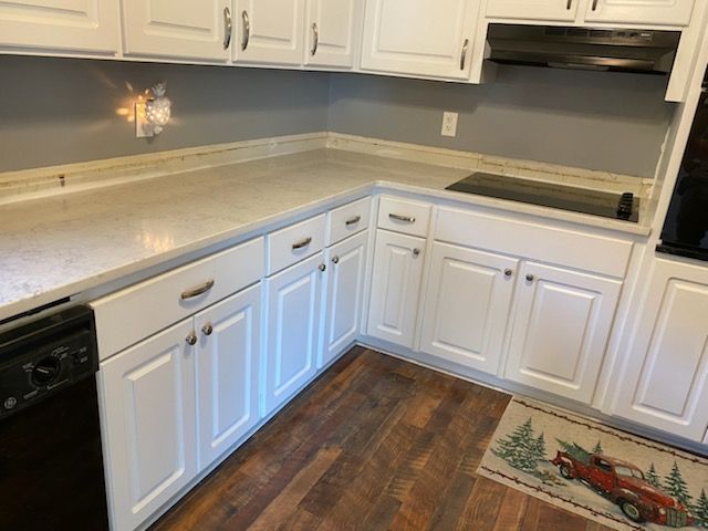 A kitchen with white cabinets , a black dishwasher , a stove and a rug with a red truck on it.
