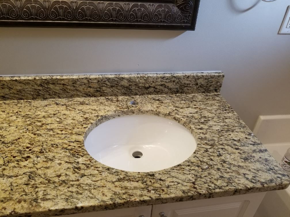 A bathroom sink with a granite counter top and a mirror.