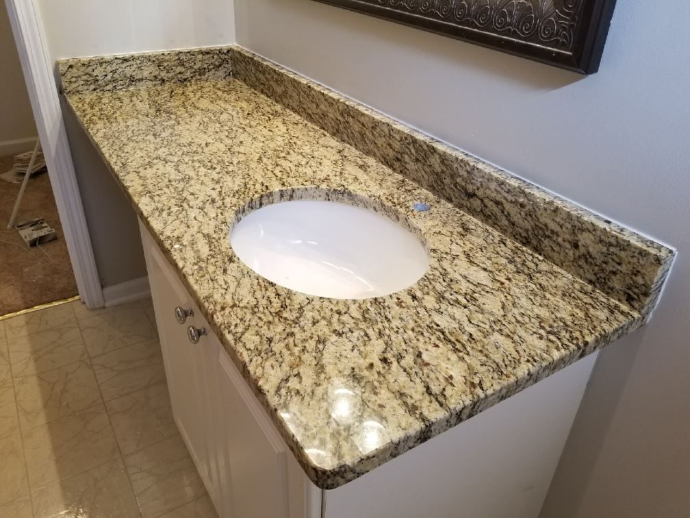 A bathroom vanity with a granite counter top and a sink.