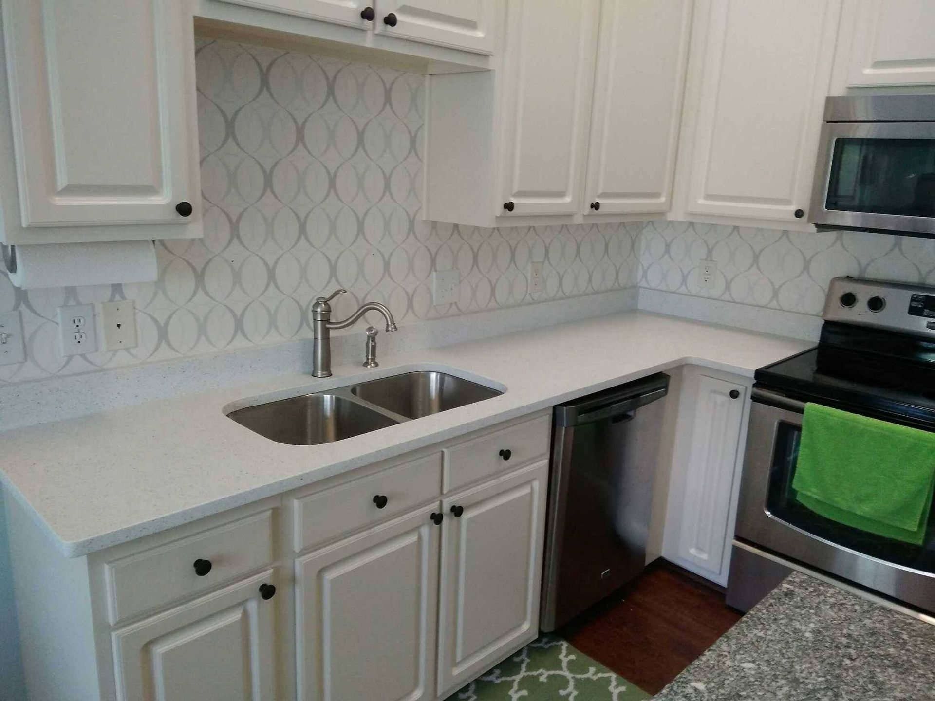 A kitchen with white cabinets , stainless steel appliances , a sink and a stove.