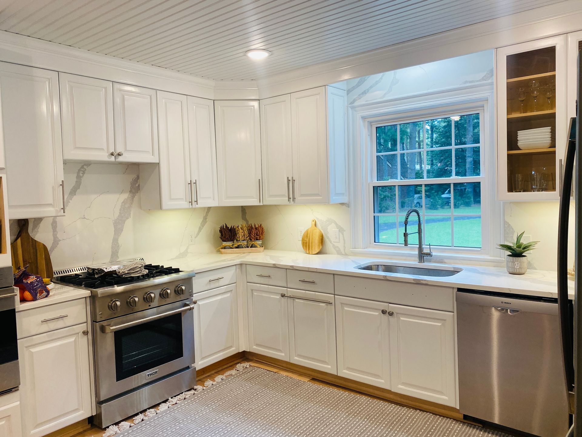 A kitchen with white cabinets , stainless steel appliances , and a large window.