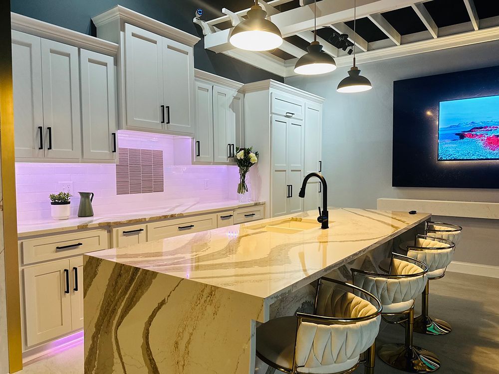 A kitchen with white cabinets , a large island , stools and a television.