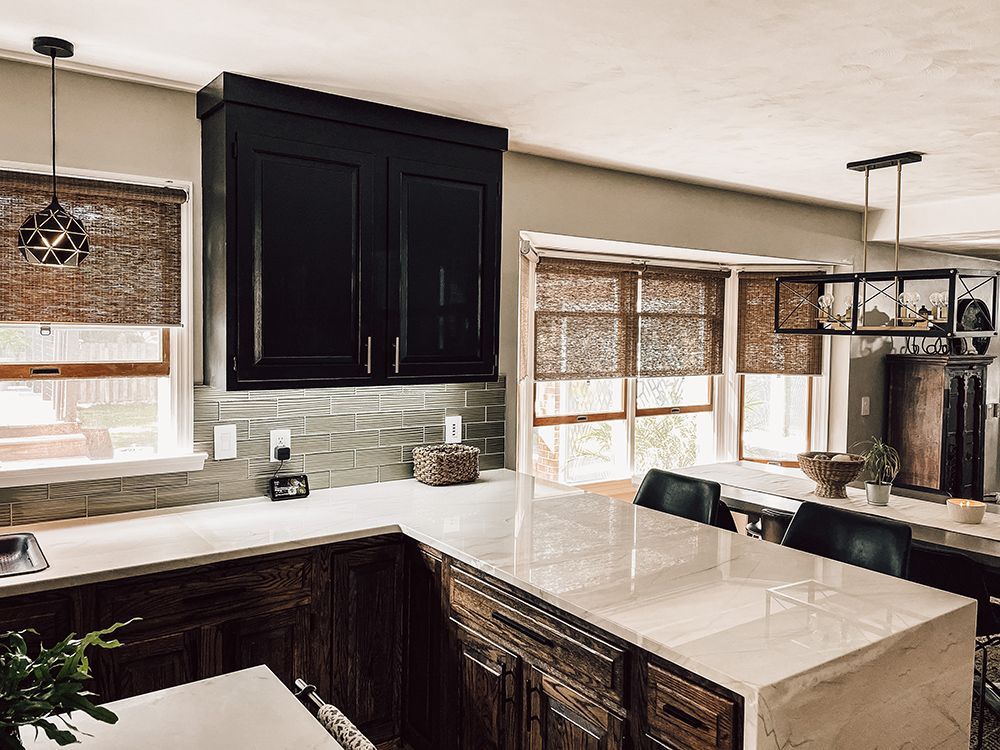 A kitchen with black cabinets , white counter tops , and a large island.