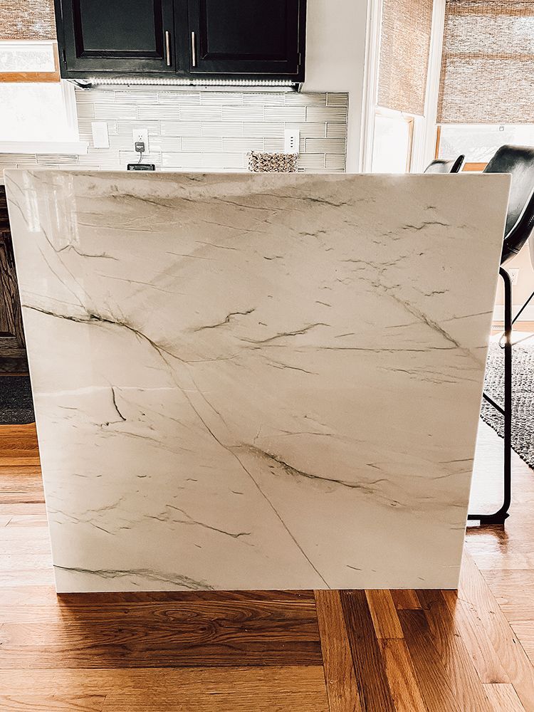 A white marble counter top is sitting on a wooden floor in a kitchen.