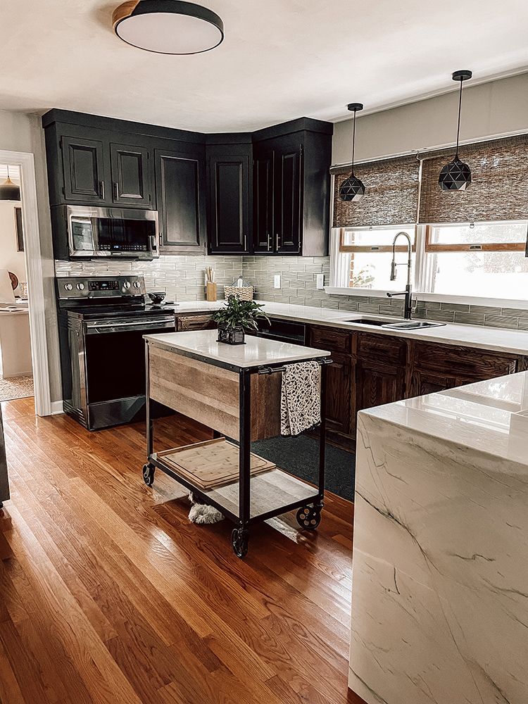A kitchen with hardwood floors , black cabinets , stainless steel appliances and a wooden island.