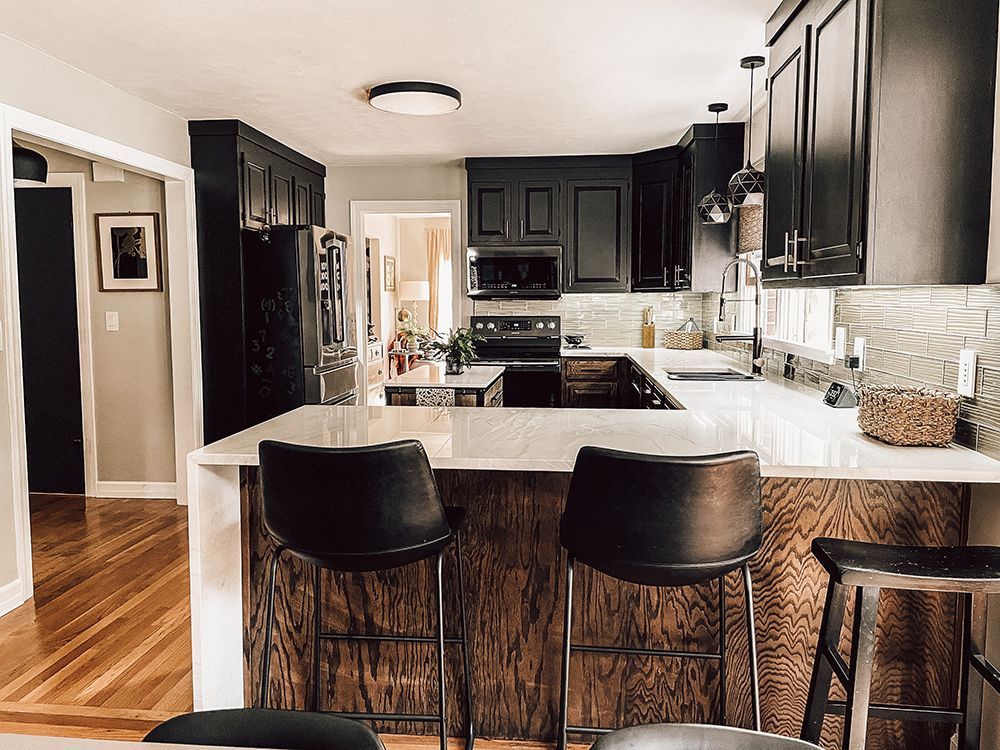 A kitchen with black cabinets , a white counter top , and two bar stools.