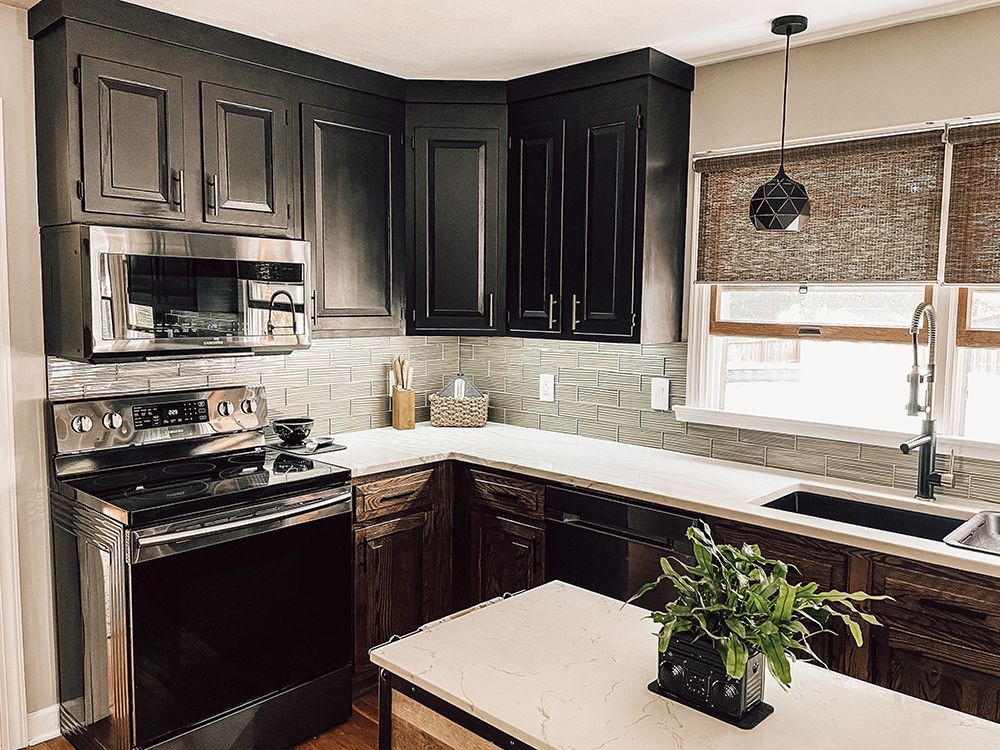 A kitchen with black cabinets , stainless steel appliances , a sink , and a microwave.