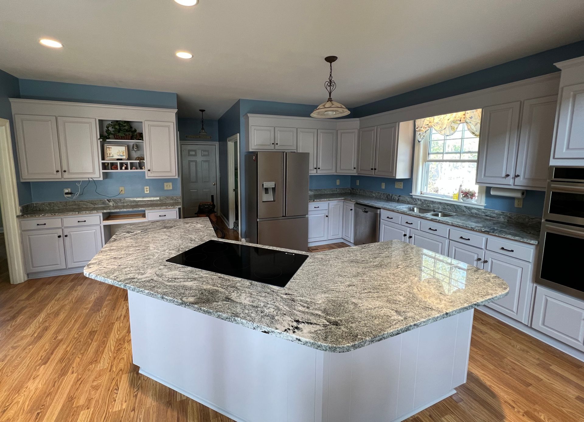A kitchen with white cabinets , granite counter tops , stainless steel appliances and a large island.