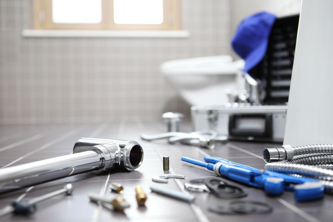 Plumbing tools scattered on floor in bathroom near a toilet and tool box.