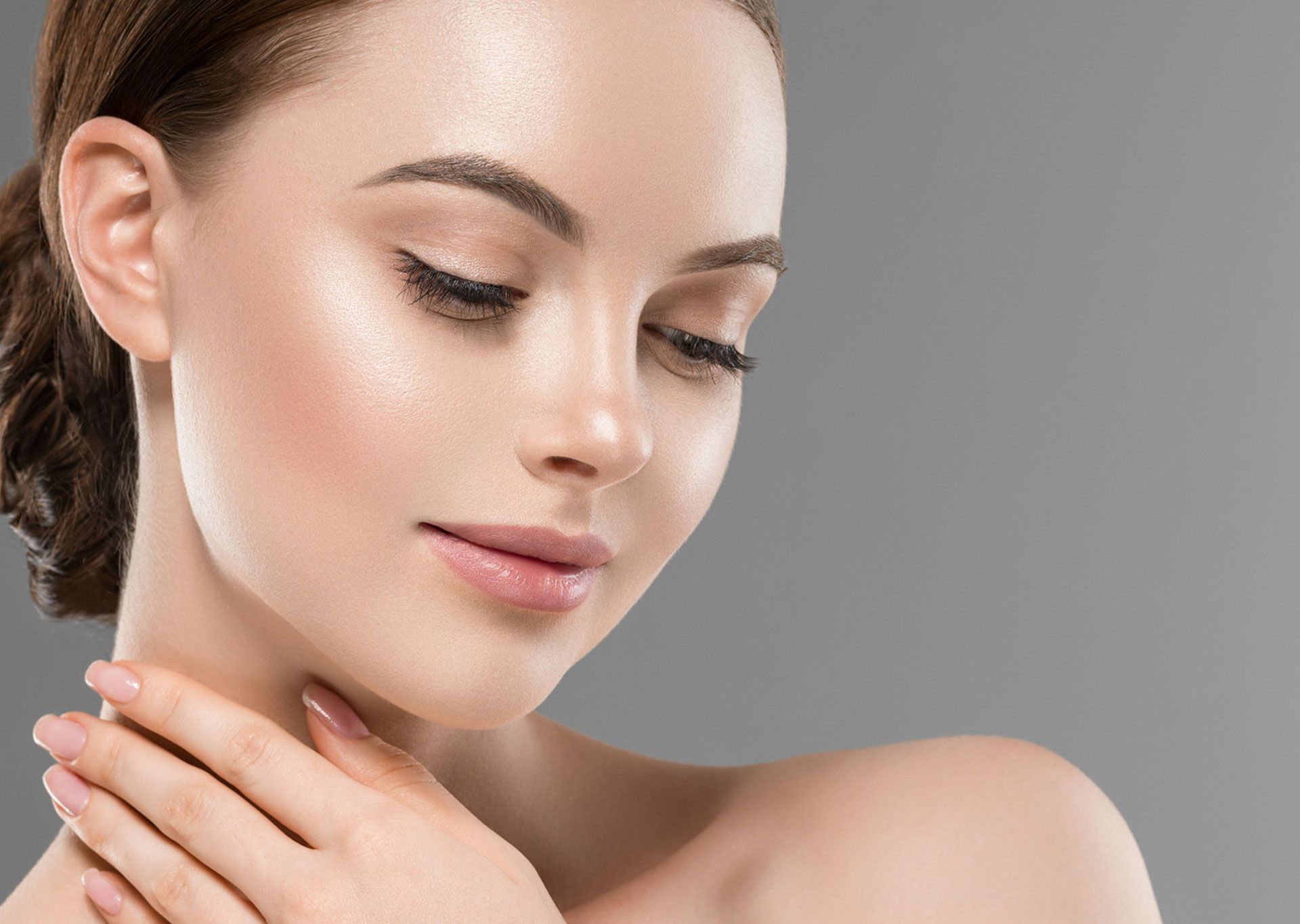 Woman with fair skin touches her neck, eyes closed, against a gray background.