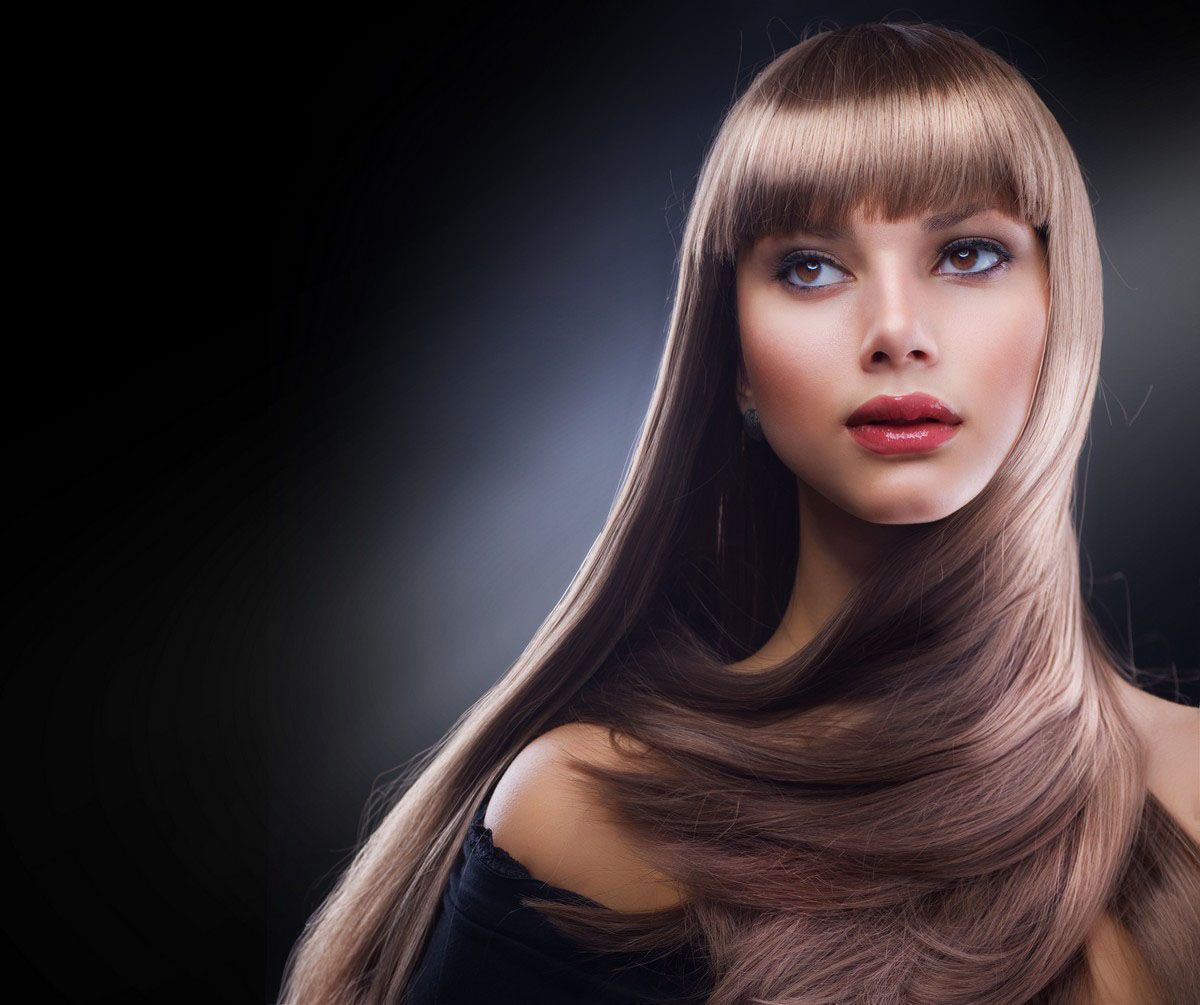Woman with long, straight brown hair and bangs, looking off-camera, against a black background.