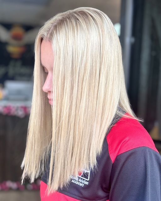 Person with long platinum-blonde hair in profile, wearing a black and red shirt indoors.