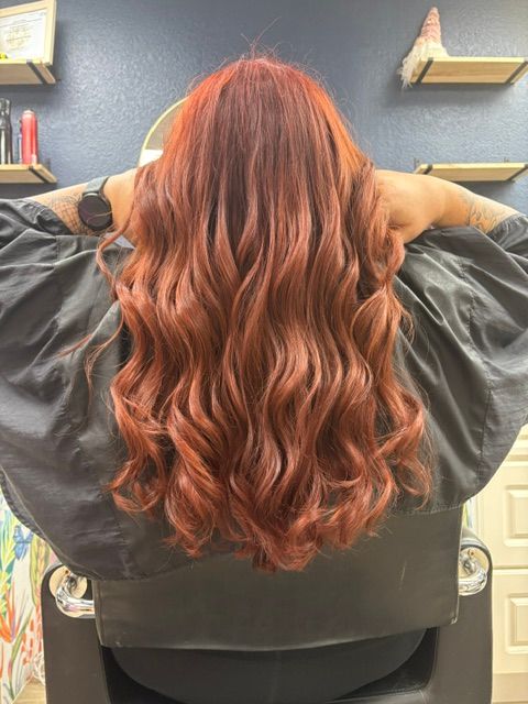 Wavy copper-red hair styled in loose curls, shown from behind in a salon chair.