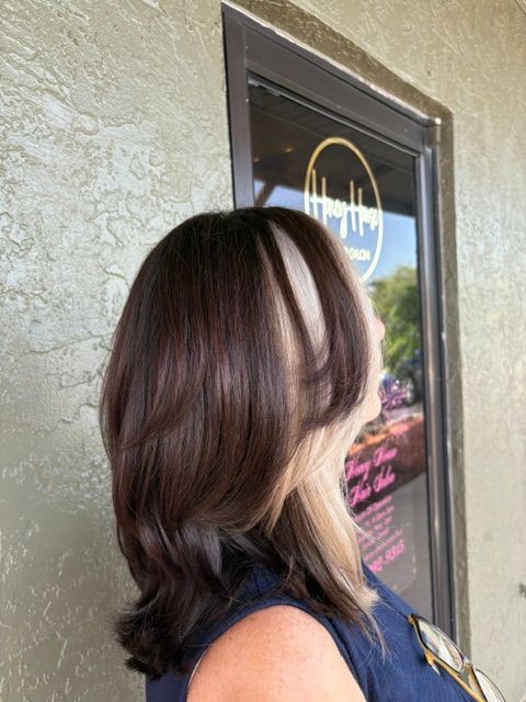 Woman with shoulder-length highlighted hair standing outside a storefront with a window sign.