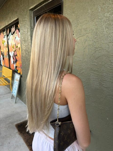 Woman with long blonde hair walking past a storefront, carrying a black purse and wearing a white dress.