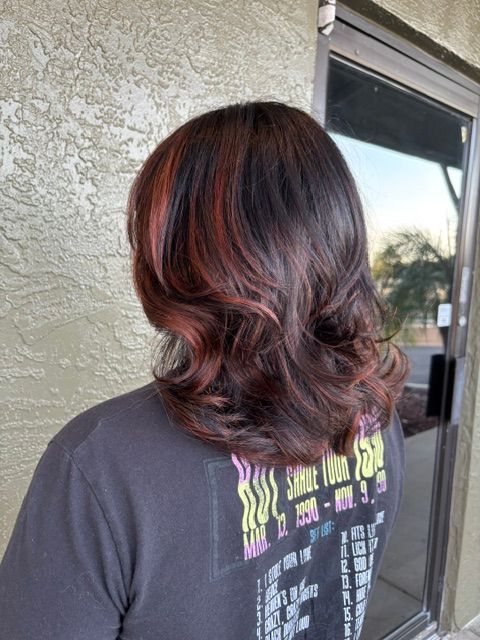 Back view of shoulder-length dark hair with red highlights, curled at the ends, outdoors by a stucco wall.