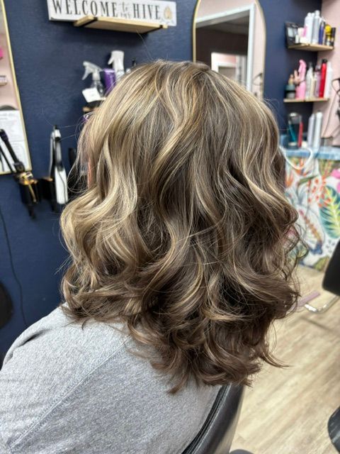 Shoulder-length wavy brown hair with blonde highlights in a salon chair