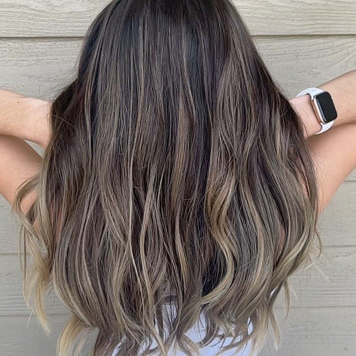 Wavy brunette hair with subtle blonde highlights, seen from the back against a gray wood wall.