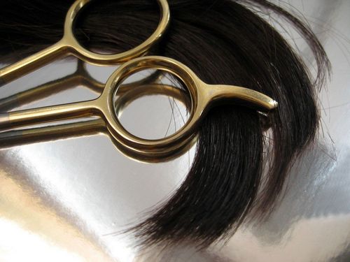 Gold scissors cutting dark brown hair on a silver surface.
