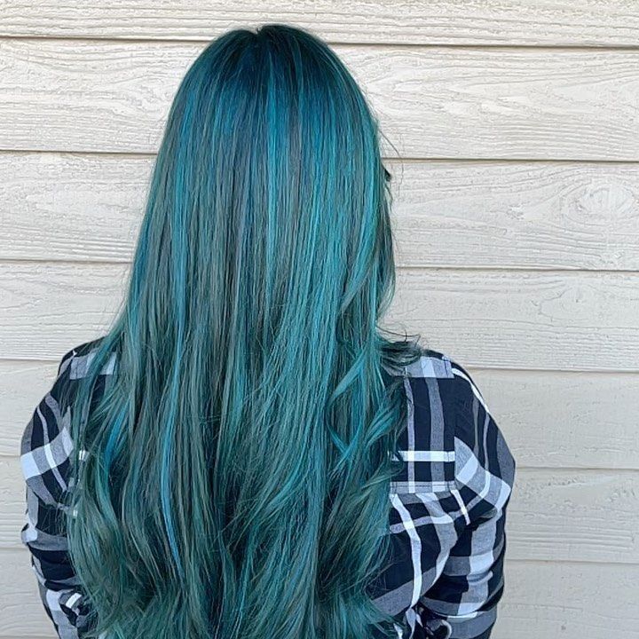 Woman with long, teal-colored hair and plaid shirt stands in front of a wood-paneled wall.