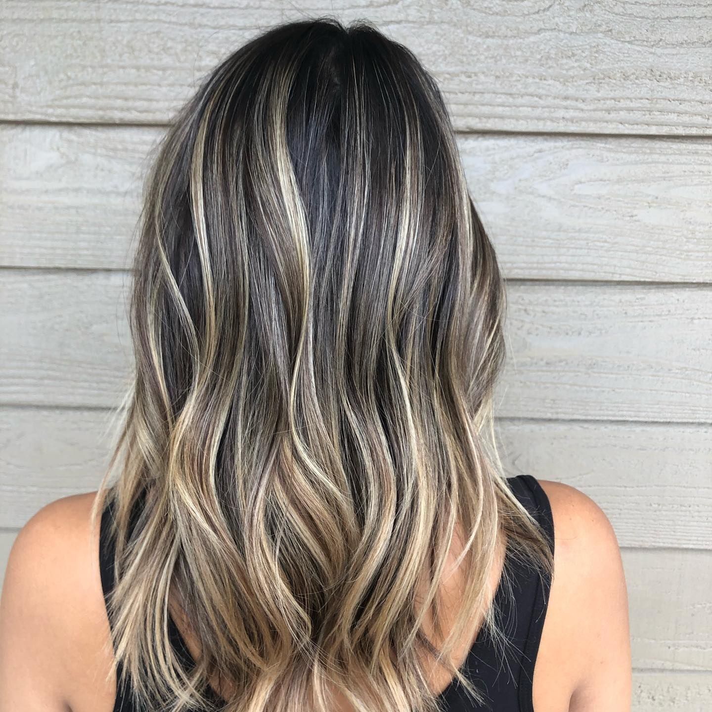 Woman with wavy, highlighted hair; dark roots fade to blonde tips.