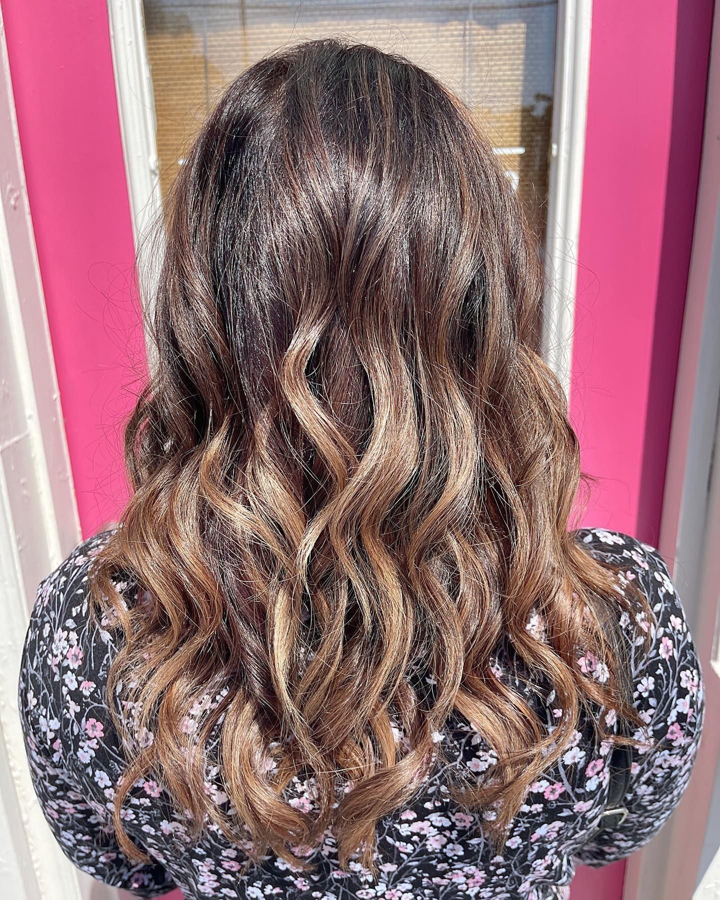 Woman with wavy brown hair, dark at the roots and lighter at the ends, wearing a floral top.
