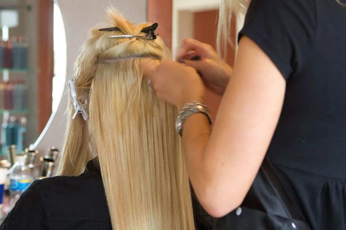 Blonde hair extensions being attached in a salon; stylist is working on the client's hair.