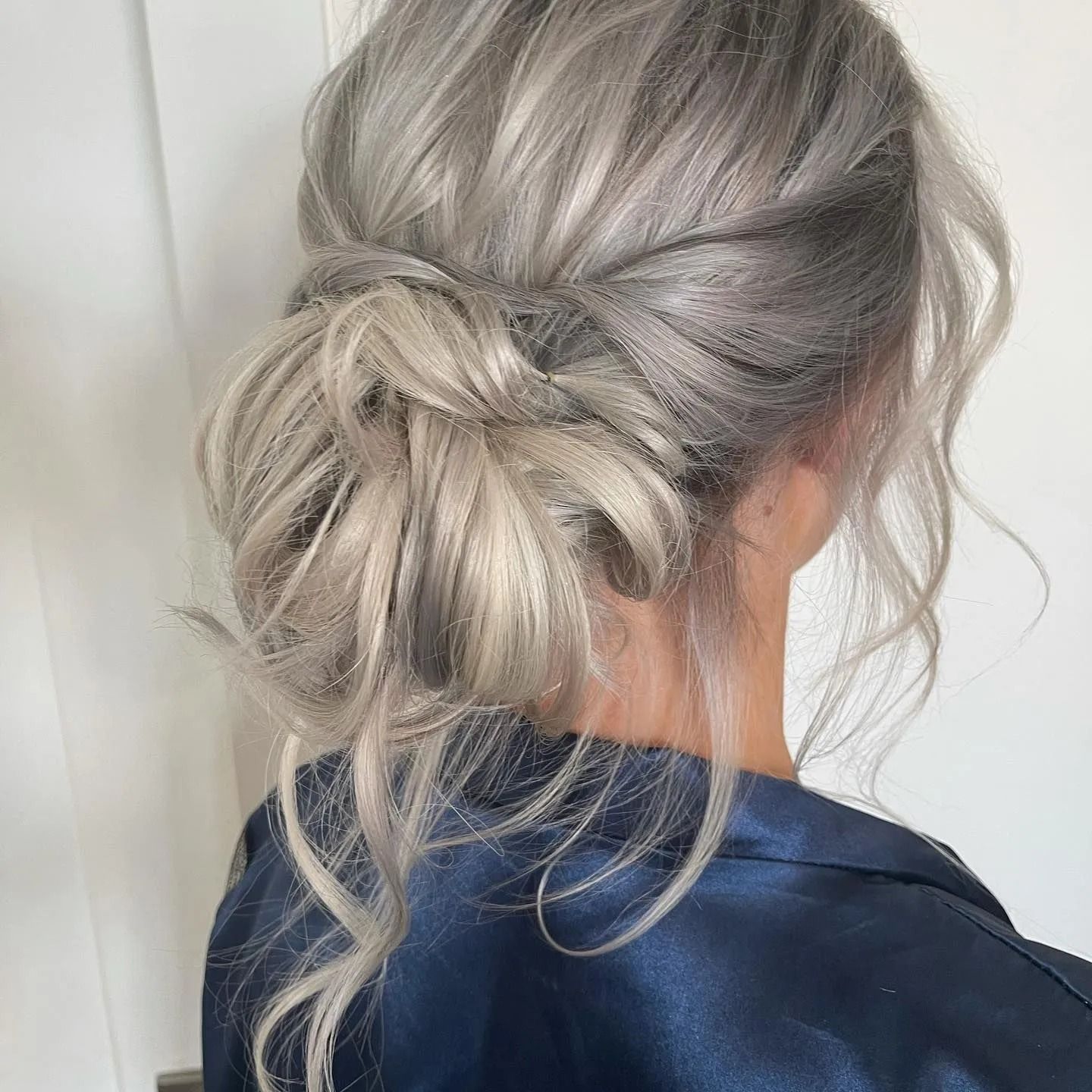 Woman with silver hair in a loose updo. Wears a dark blue satin robe.