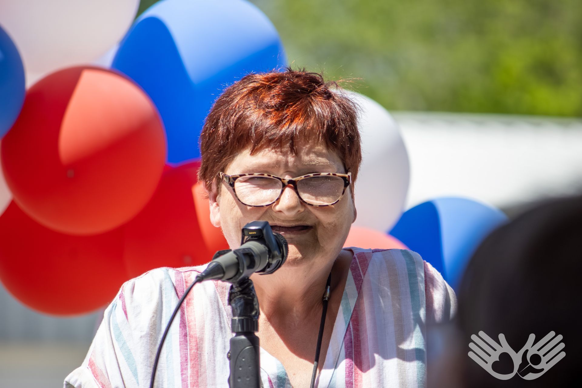 Woman speaking into a microphone with red, white, and blue balloons in the background