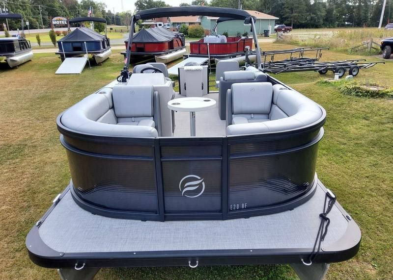 A black and gray pontoon boat is parked in a grassy field.