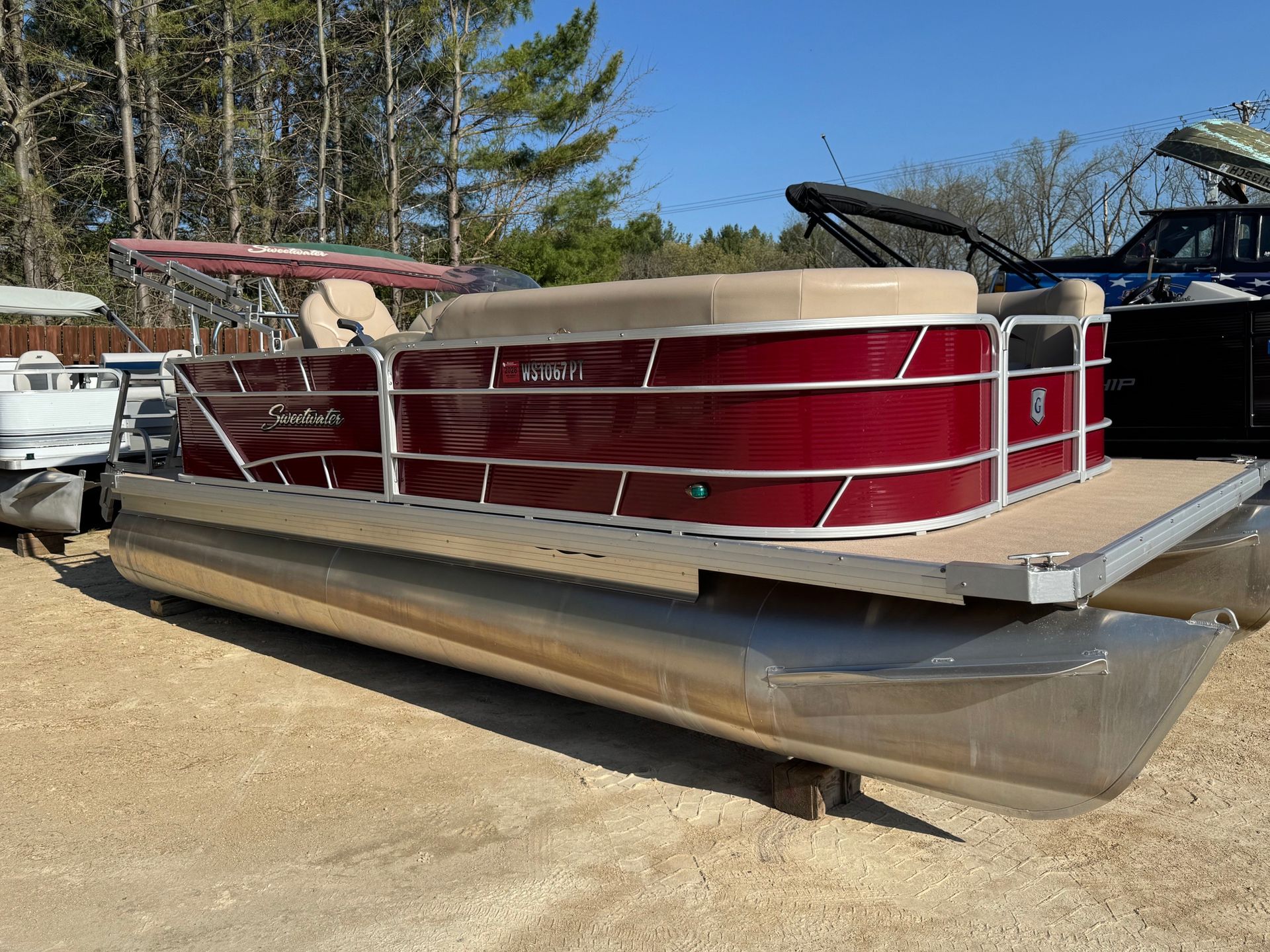 A red pontoon boat is parked in a lot next to a truck.