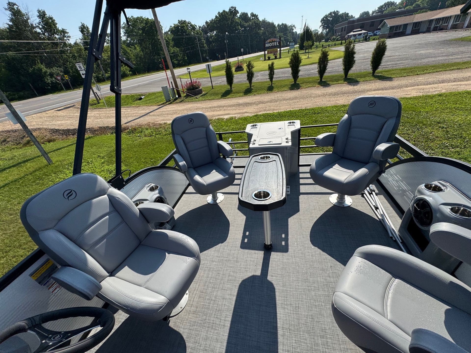 A view of the grey, carpeted deck of a pontoon boat, featuring four grey swivel captain's chairs and a central table.