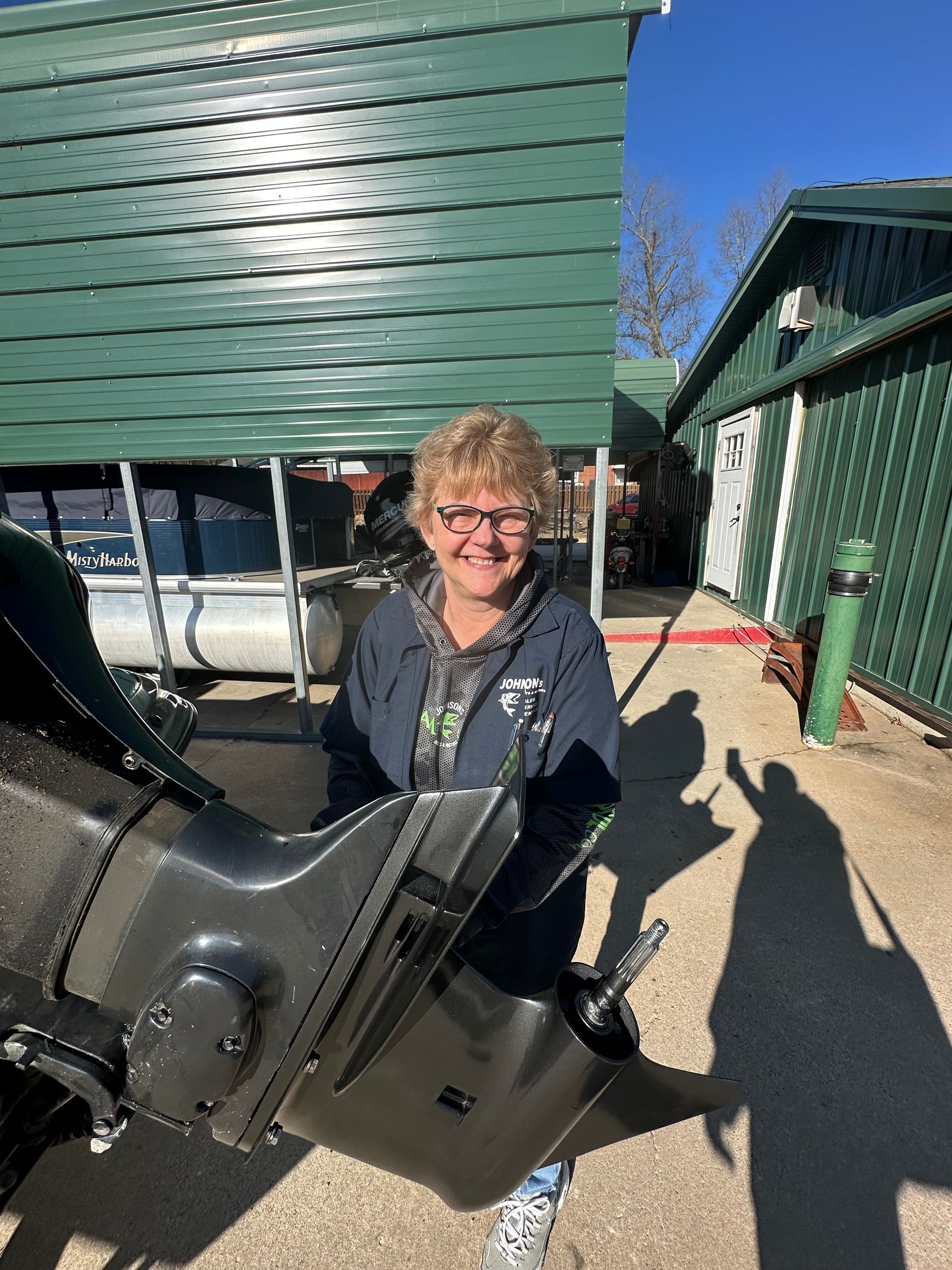 A woman is holding a boat engine in front of a green building.