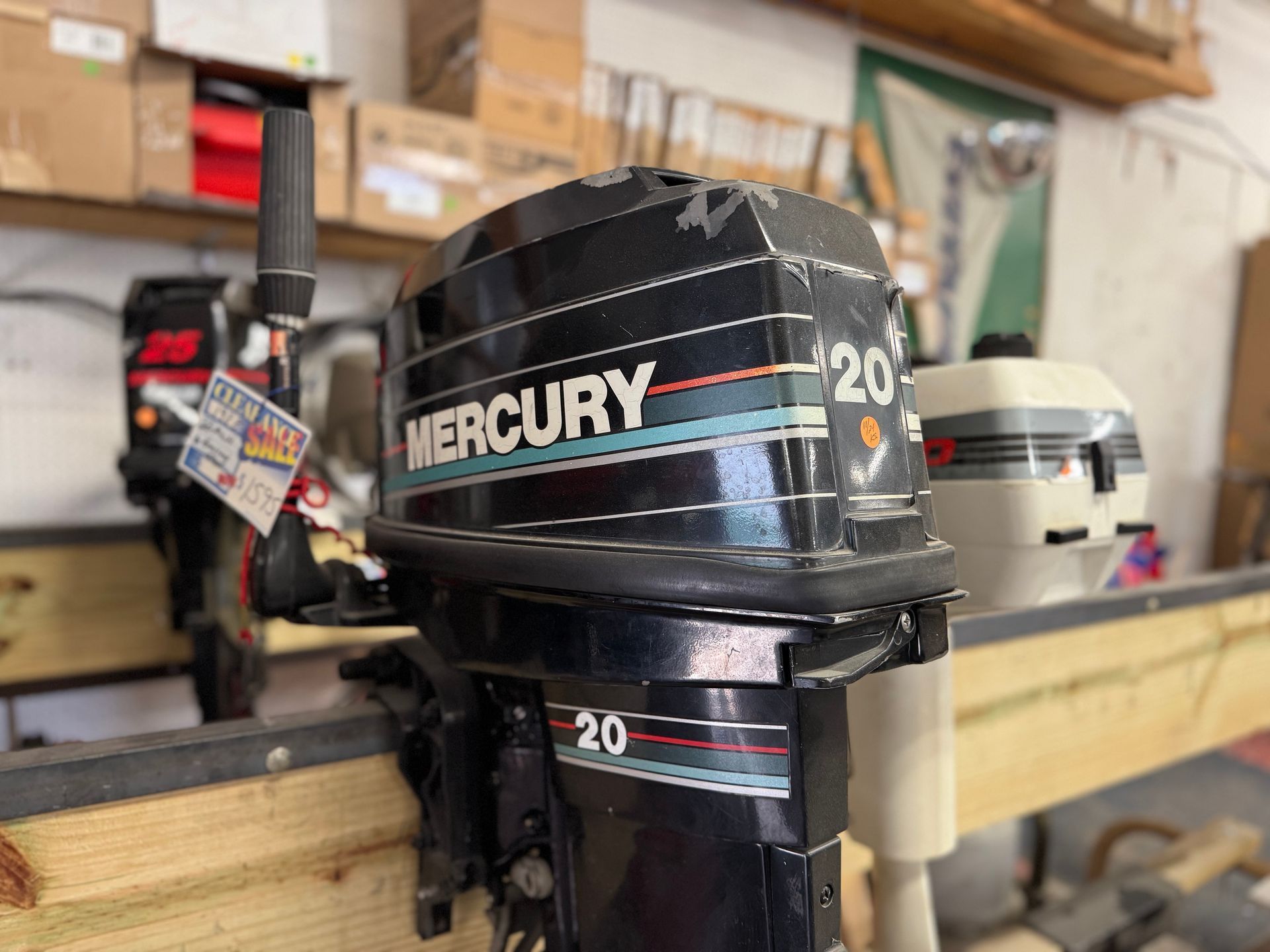 Black Mercury 20 outboard motor with a blue and red stripe; displayed in a workshop setting.