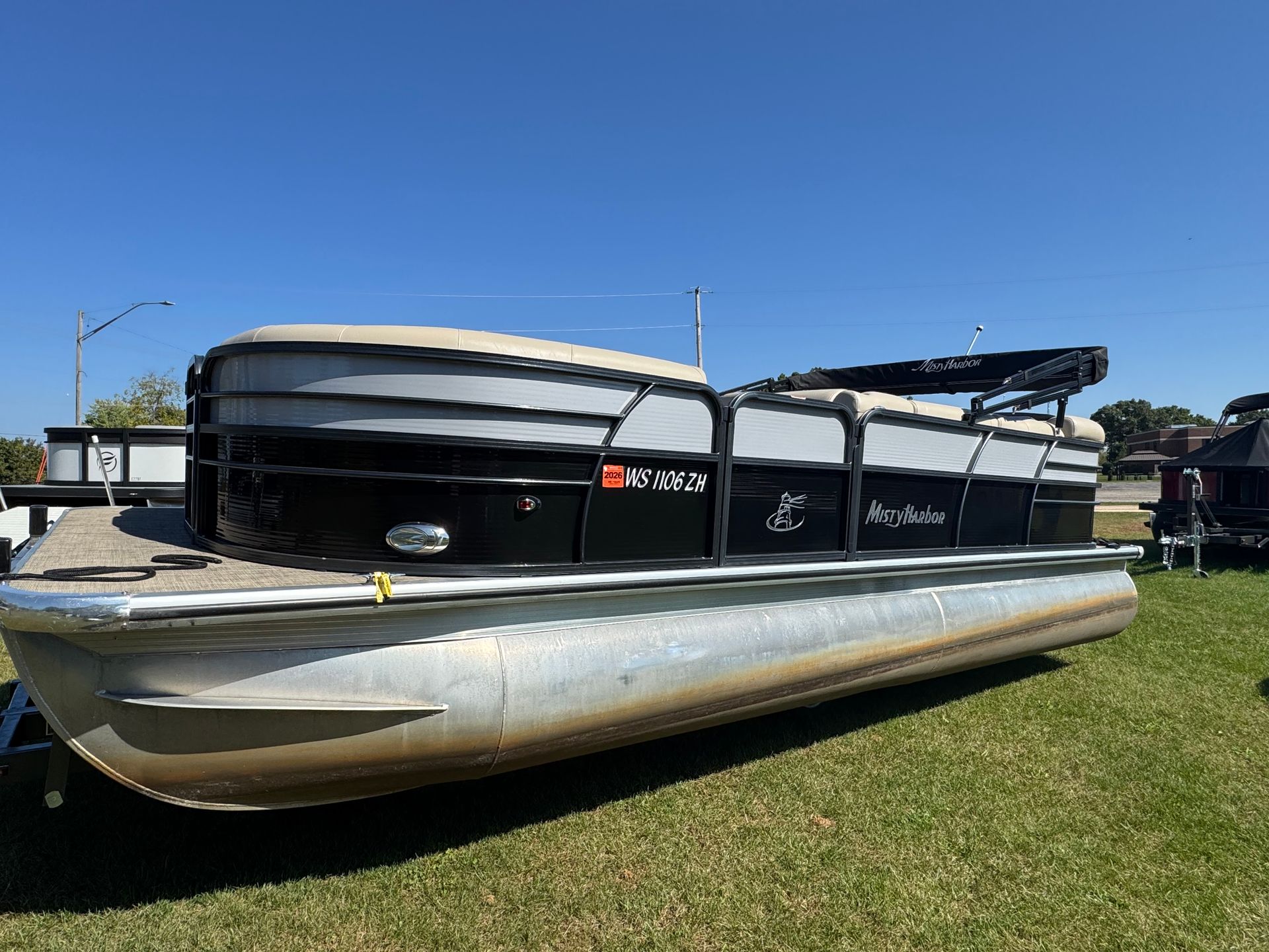 Pontoon boat on a grassy lawn under a clear blue sky.