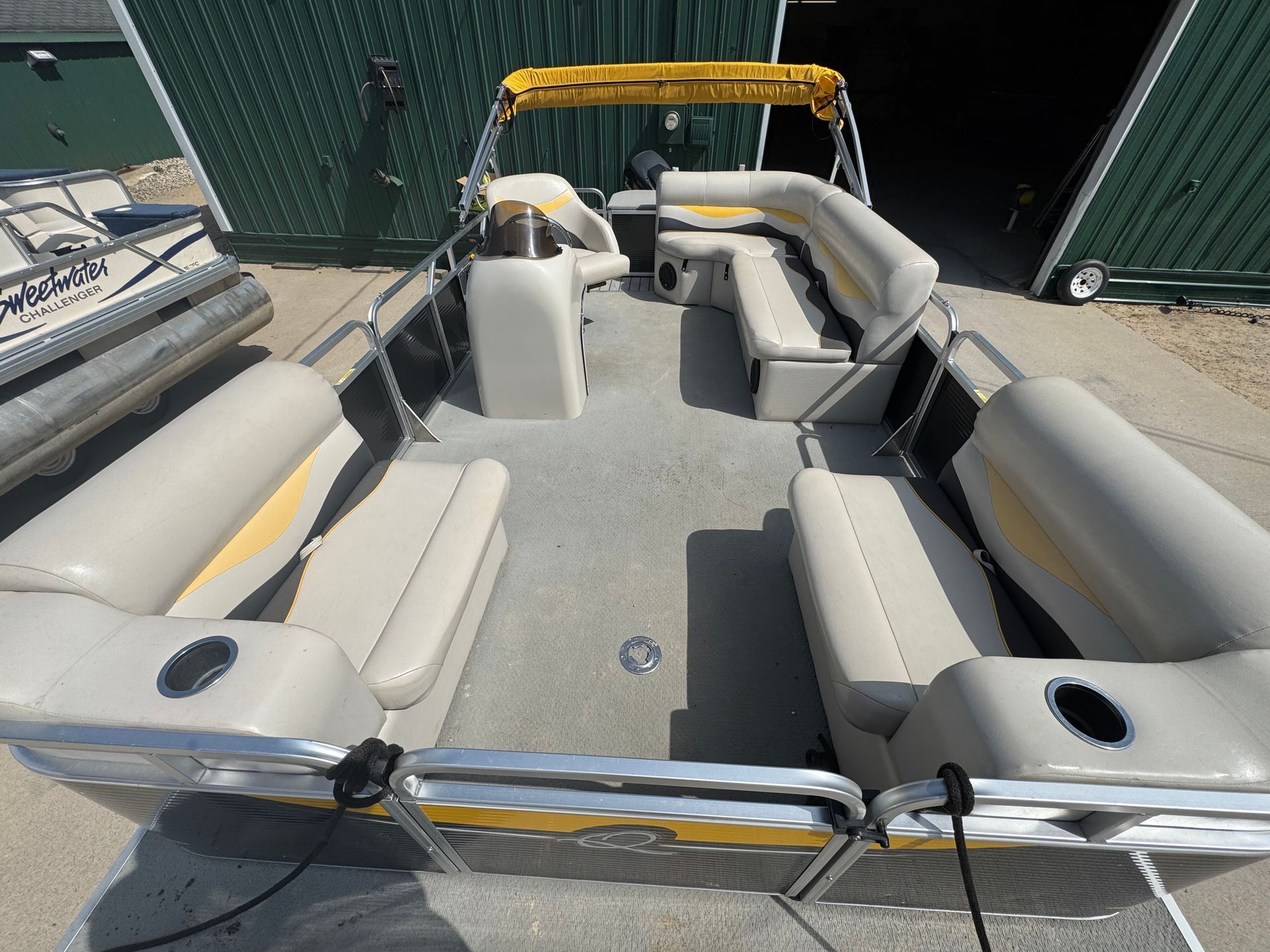 Pontoon boat with beige and yellow seating, parked outdoors.