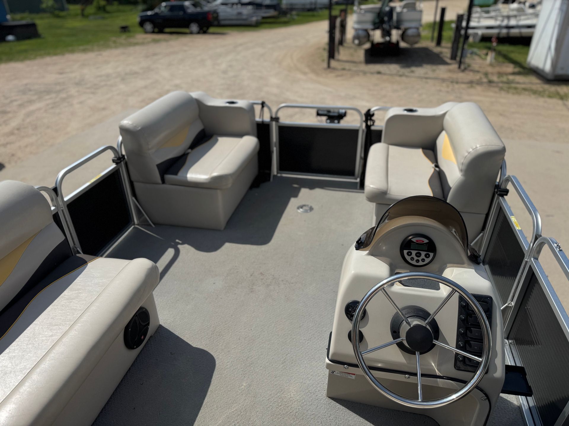 Interior view of a beige pontoon boat with steering wheel, seating, and cup holders.