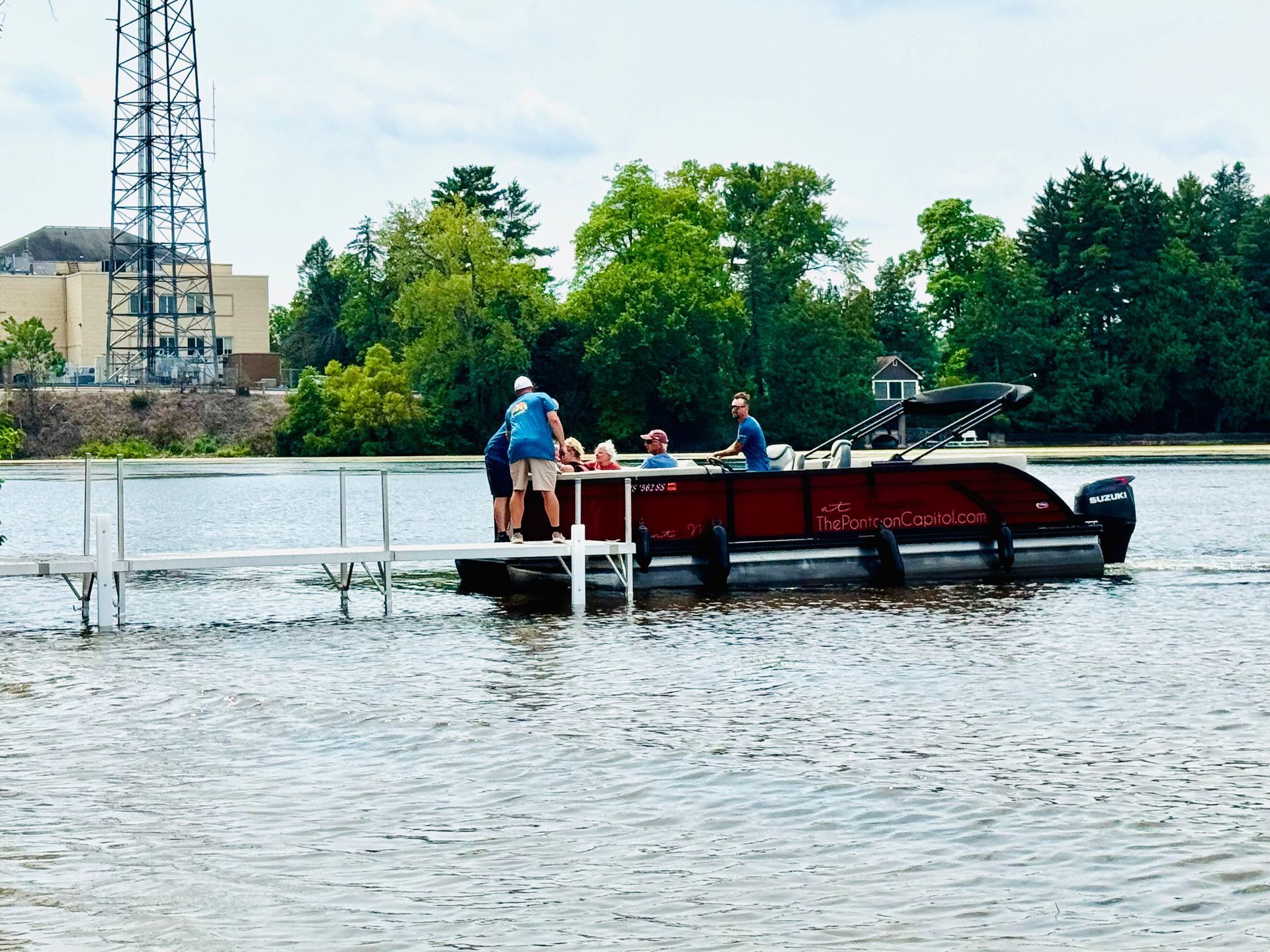 Red pontoon boat with people, docked on a lake, near a pier.