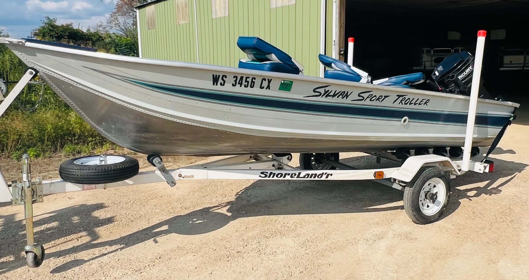 A boat is on a trailer in front of a garage.